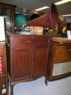 This Auxetophone is in the 'Queen Anne' Style with a highly polished mahogany cabinet with panelled doors and cabriole legs. It has a triple-spring spiral-drive motor, 12" turntable, speed indicator, tapering tone-arm with gooseneck, auxetophone soundbox, and a mahogany grained Flaxite horn. Part of the EMI Group Archive Trust collection 
